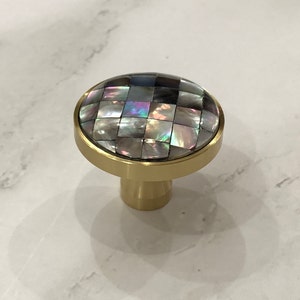 May include: A round, gold-toned cabinet knob with a decorative top made of iridescent mother-of-pearl tiles.