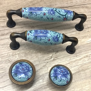 Può includere: Set di tre pomelli per armadi in ceramica con un design floreale blu e bianco. I pomelli hanno una finitura in bronzo e sono di diverse dimensioni.