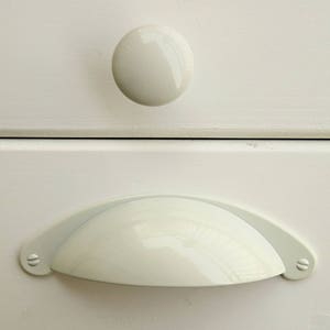 May include: White ceramic drawer pull with a rounded, half-circle shape. The pull has two small, round screw holes on either side.