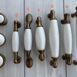 May include: Assortment of 9 cabinet knobs and pulls in a brushed brass finish with white ceramic inserts featuring a geometric pattern.