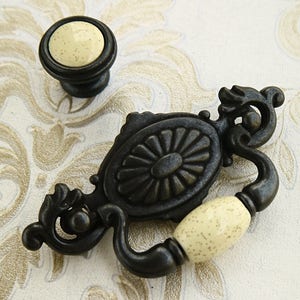 May include: Black metal drawer pull with an ornate design and two off-white ceramic knobs.