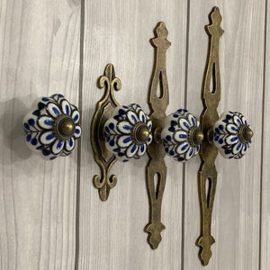 May include: Four white ceramic knobs with blue floral designs, attached to three antique gold metal hooks.