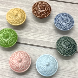 Könnte beinhalten: Satz von zehn Keramik-Schrankknöpfen mit Blumenmuster. Die Knöpfe sind in verschiedenen Farben, darunter Grün, Blau, Gelb, Rosa und Braun.
