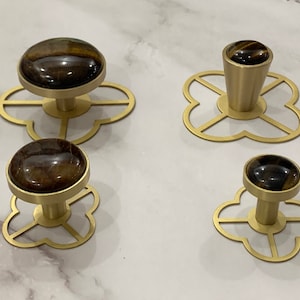 May include: Four gold-toned cabinet knobs with a flower-shaped base. Each knob features a round, brown tiger's eye stone.