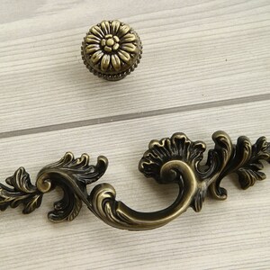 May include: A pair of antique-style cabinet pulls with a floral design. The pulls are made of metal and have a dark bronze finish.
