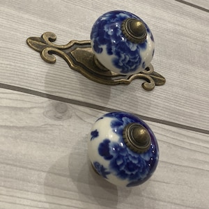 May include: Two blue and white porcelain cabinet knobs with a floral design. The knobs are attached to a decorative brass plate.