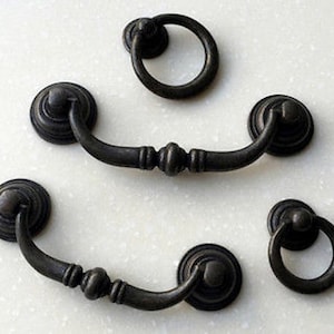 May include: Five antique-style cabinet hardware pulls in a black finish. Two are ring pulls, and three are arched pulls with a decorative knob at the top.