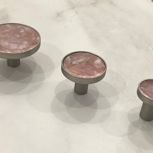 May include: Three round cabinet knobs with a pink marbled finish and a silver base.