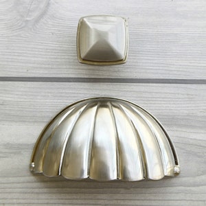 Peut inclure: Deux boutons de cabinet en nickel brossé. L'un est un bouton carré avec un centre surélevé et l'autre est un bouton demi-rond avec un motif cannelé.