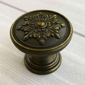 May include: A round, antique brass cabinet knob with a decorative floral design.