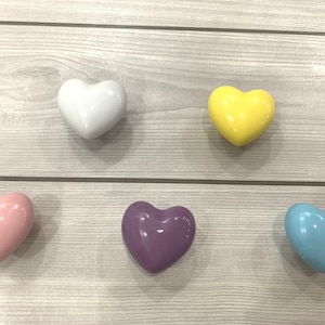 May include: Five ceramic heart-shaped drawer pulls in different colors: white, yellow, pink, purple, and light blue.