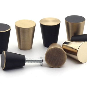 Pode incluir: Um conjunto de oito botões de armário em dois acabamentos: preto e latão. Os botões são em forma de cone com uma parte superior arredondada.