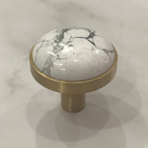 Op de afbeelding: Een witte marmeren kastknop met een gouden metalen basis.