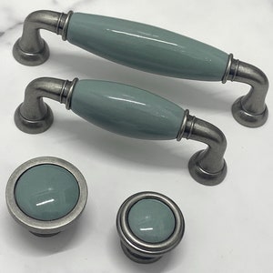 May include: Set of four cabinet knobs and pulls in a light blue ceramic with a pewter finish. The knobs and pulls have a rounded, oval shape.