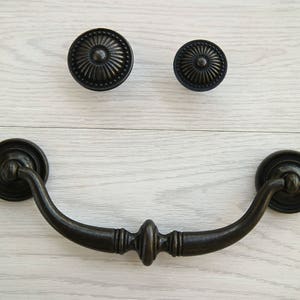 May include: Black metal cabinet hardware with a decorative design. The hardware includes a pull handle and two knobs.