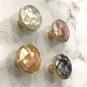 Pode incluir: Quatro botões redondos para armário com base de metal dourado e uma incrustação decorativa de concha iridescente. Os botões são de quatro cores diferentes: branco, rosa, amarelo e preto.