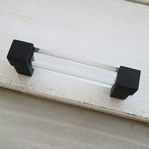 May include: A black and clear glass cabinet pull with square ends.