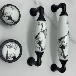 Op de afbeelding: Twee zwarte en witte keramische kastknoppen met een bloemenmotief en twee bijpassende zwarte en witte keramische kastgrepen met een bloemenmotief.