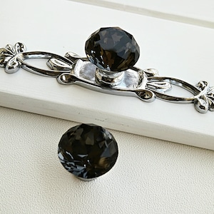 Pode incluir: Um par de botões decorativos para armário com acabamento prateado e design de cristal cinza escuro.