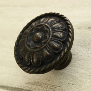 Może przedstawiać: Okrągły, ozdobny, brązowy gałka do szafki z kwiatowym wzorem. Gałka ma sznurkowy brzeg wokół krawędzi.