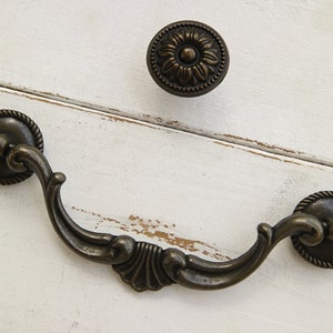 May include: A pair of antique-style cabinet hardware pulls in a brass finish. One pull is a round knob with a floral design, and the other is a curved handle with a decorative scroll design.