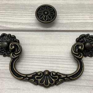 May include: A set of two ornate, antique-style cabinet pulls with a floral design. The pulls are made of metal and have a dark bronze finish.