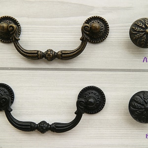 Op de afbeelding: Vier kastknoppen, twee zijn zwart en twee zijn brons. De knoppen zijn versierd met een bloemmotief. De knoppen zijn gemarkeerd met A, B, C en D.