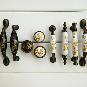 Pode incluir: Conjunto de botões e puxadores de armário de latão antigo com desenhos florais. Os botões são redondos e os puxadores são ovais. Os desenhos florais são em tons de dourado e preto.
