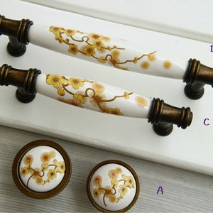 May include: Four ceramic cabinet knobs with a floral design. The knobs are white with a yellow floral pattern. The knobs have a bronze finish.