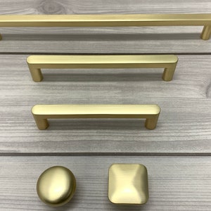 May include: Four gold cabinet hardware pulls in different sizes and styles. The pulls include three rectangular bar pulls and one round knob.
