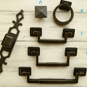 May include: Assortment of antique bronze cabinet hardware, including a square knob, a ring pull, and four different styles of drawer pulls.
