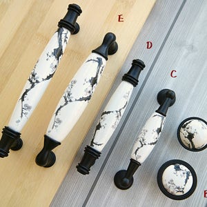 May include: Six black and white ceramic cabinet knobs with a floral design. The knobs are in various sizes and shapes, including round and oval. The knobs are on a wooden surface.