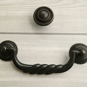 May include: Black metal drawer pull with a twisted design and a matching black metal knob.