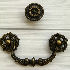 May include: A pair of ornate, antique-style cabinet pulls with a decorative floral design. The pulls are made of metal and have a brass finish.