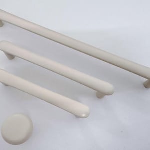 Op de afbeelding: Een set van vier crèmekleurige kastbeslagen. De set bevat drie stanggrepen van verschillende lengtes en een ronde knop. De hardware heeft een gladde, matte afwerking en een minimalistisch ontwerp, geschikt voor diverse meubelstijlen.