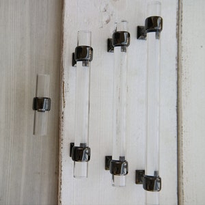 May include: Four clear glass cabinet pulls with black metal end caps. The pulls are different lengths.