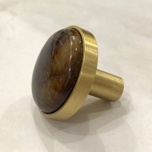 May include: A gold-toned cabinet knob with a round, brown and gold agate stone inlay.