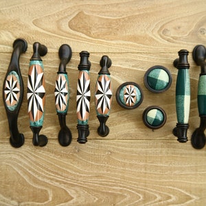 Peut inclure: Assortiment de boutons et de poignées de cabinet décoratifs avec des bases en métal noir et des dessus en céramique colorés. Certains présentent un motif géométrique en forme d'étoile éclatante en blanc, noir et vert, tandis que d'autres ont un motif à carreaux vert et blanc.