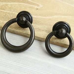 May include: Two antique bronze ring pulls with a circular design. The ring pulls have a smooth, aged finish and are perfect for adding a touch of vintage charm to cabinets, drawers, or doors.