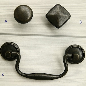 Op de afbeelding: Drie antieke stijl deurknoppen van zwart metaal. Eén is rond, één is vierkant en één is een trekknop.