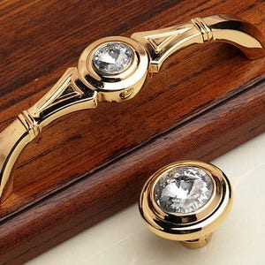 Pode incluir: Ferragens de armário douradas com um botão de cristal e uma puxador com detalhes de cristal.