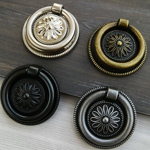 Puede incluir: Cuatro tiradores decorativos para puertas de armario con diseño de anillo. Los tiradores están en diferentes acabados: plata, latón, negro y plata antigua.