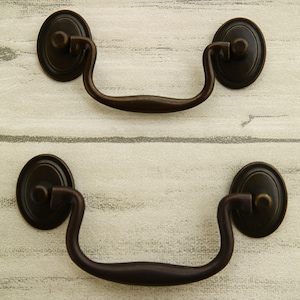 Peut inclure: Deux poignées de tiroir en bronze antique avec une poignée incurvée et des plaques ovales.