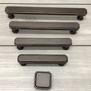 May include: Five brushed nickel cabinet pulls in various sizes, including a small knob. The pulls have a rectangular shape with rounded edges and a slightly raised centre.