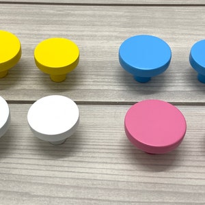 May include: Assortment of round wooden knobs in various colors, including yellow, blue, white, and pink. The knobs are all the same size and shape, and they have a smooth, polished finish.