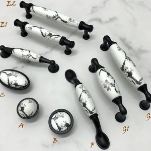 Könnte beinhalten: Sortiment aus zehn schwarzen und weißen Keramik-Schrankknöpfen mit Blumendesigns. Die Knöpfe sind mit A bis G2 beschriftet.