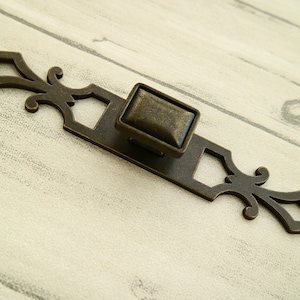 Peut inclure: Tiroir en laiton antique avec un design orné. La poignée a un bouton carré et une plaque décorative avec des découpes.