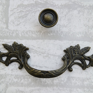 May include: A decorative antique-style cabinet pull with a floral design. The pull is made of metal and has a dark bronze finish.
