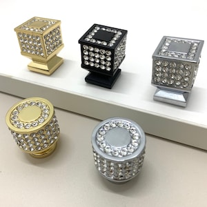 May include: Four decorative cabinet knobs with a square and round shape. The knobs are covered in rhinestones and come in gold, black, silver, and chrome finishes.