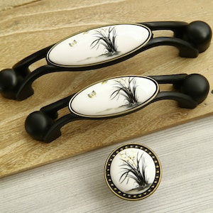 Peut inclure: Trois boutons de cabinet en céramique noire et blanche avec un motif floral. Les boutons sont de forme ovale et ont une base en métal noir. Le plus petit bouton est rond.